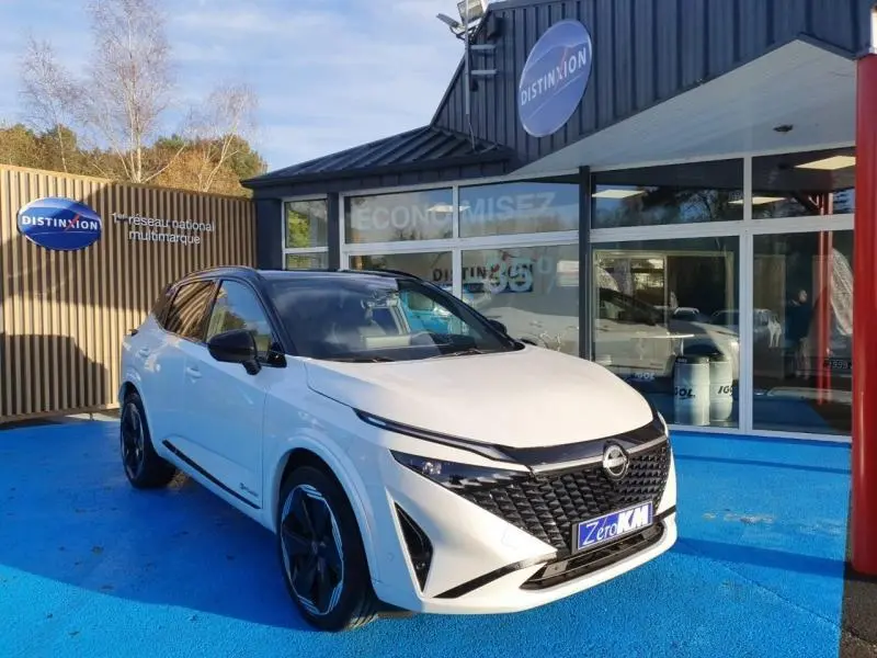 Nissan Qashqai Hybrid e-POWER 2025 blanc nacré toit noir, vue 3/4 avant sur sol bleu devant showroom Distinxion