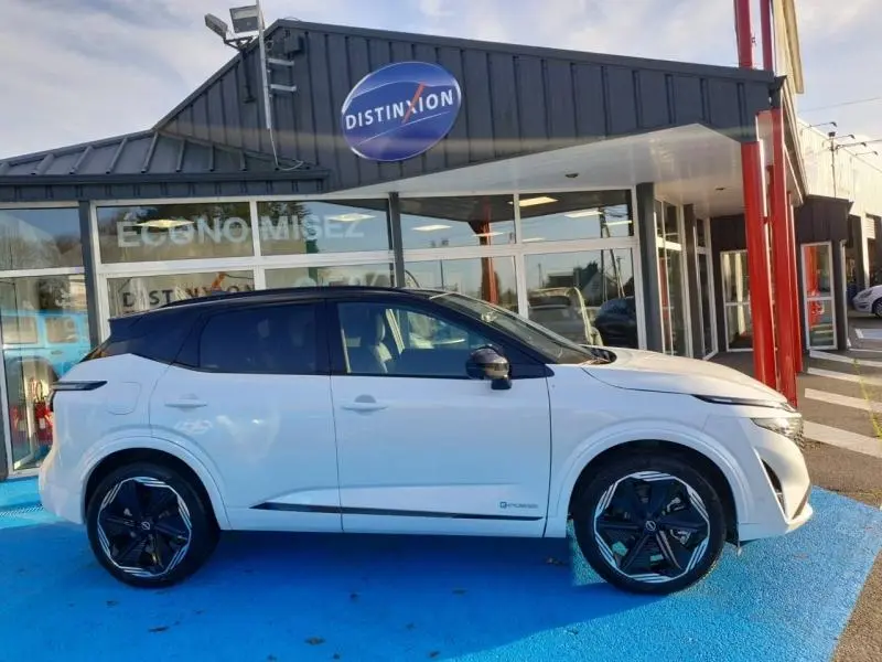 Profil côté gauche du Nissan Qashqai Hybrid e-POWER blanc nacré avec toit noir, stationné devant un showroom.