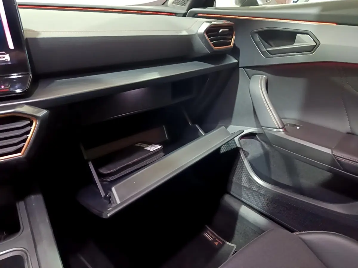 Intérieur côté passager du CUPRA Formentor gris foncé 2024, avec boîte à gants ouverte et détails en cuir et aluminium.