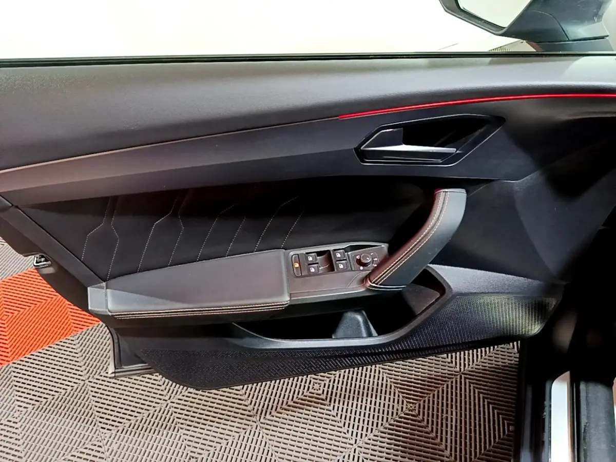 Vue intérieure du panneau de porte côté gauche de la CUPRA Formentor gris foncé, avec commandes électriques et surpiqûres rouges.