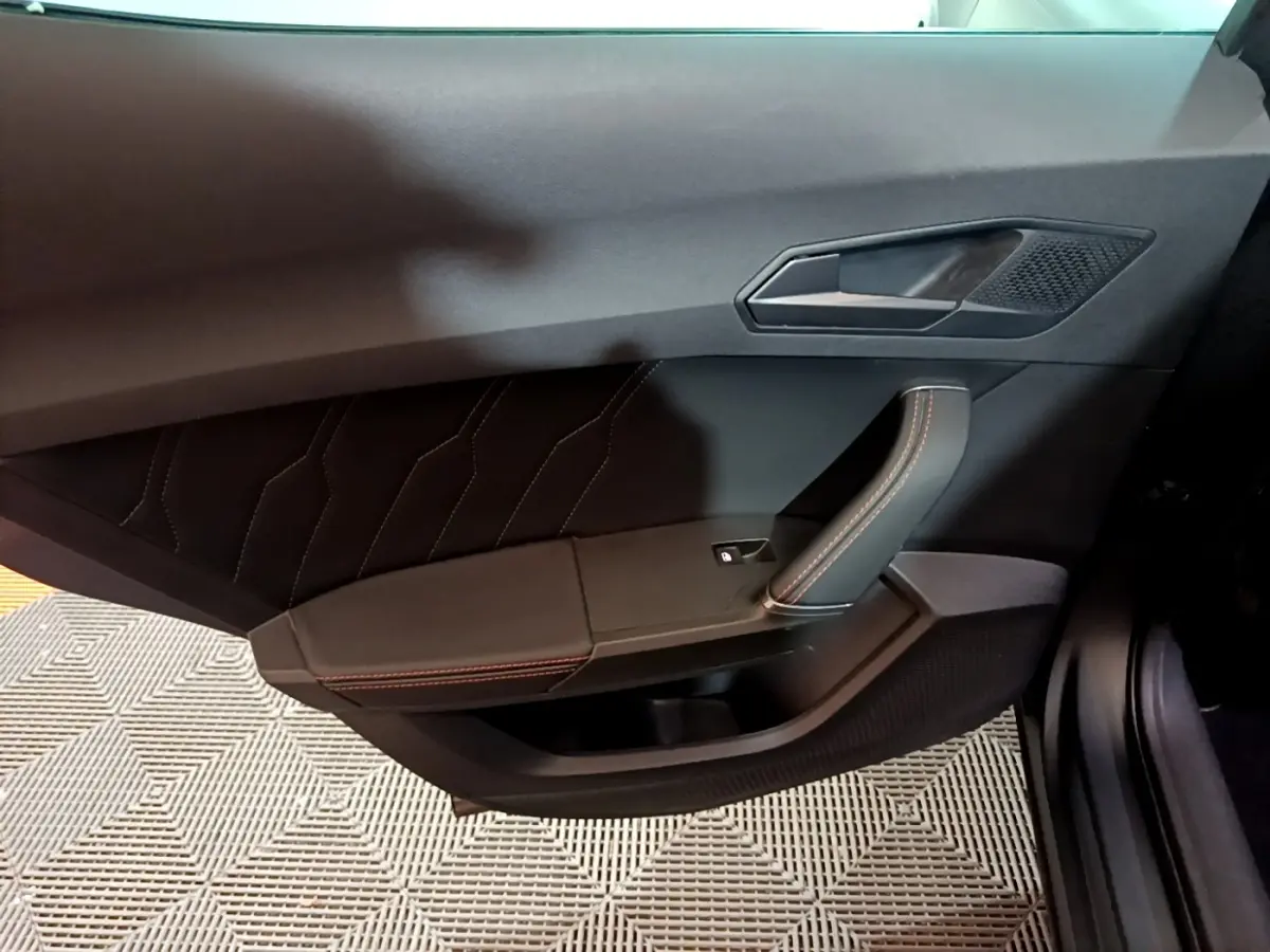 Vue intérieure côté gauche de la porte avant d'une CUPRA Formentor gris foncé avec surpiqûres rouges et poignée en cuir.