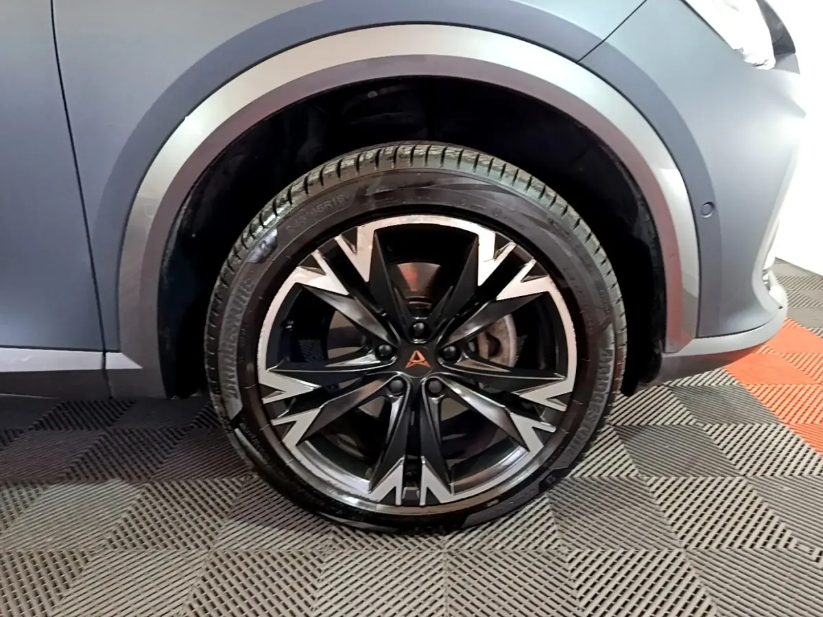 Gros plan sur la roue avant droite du CUPRA Formentor gris foncé, mettant en valeur la jante alu noire et argentée au design dynamique.