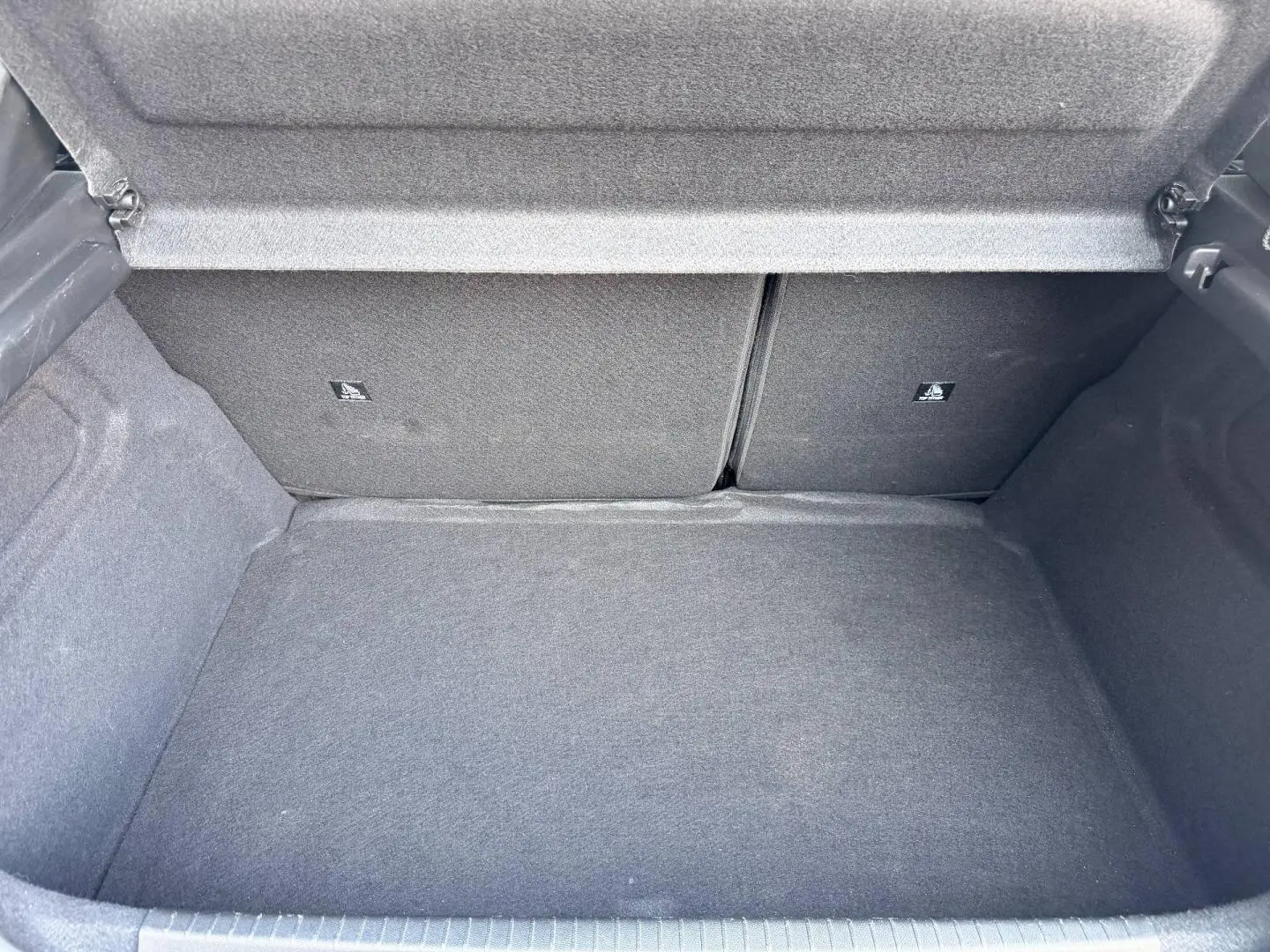 Coffre ouvert de Peugeot 208 1.2 100ch Allure, vue intérieure montrant la moquette grise et la banquette arrière rabattable.