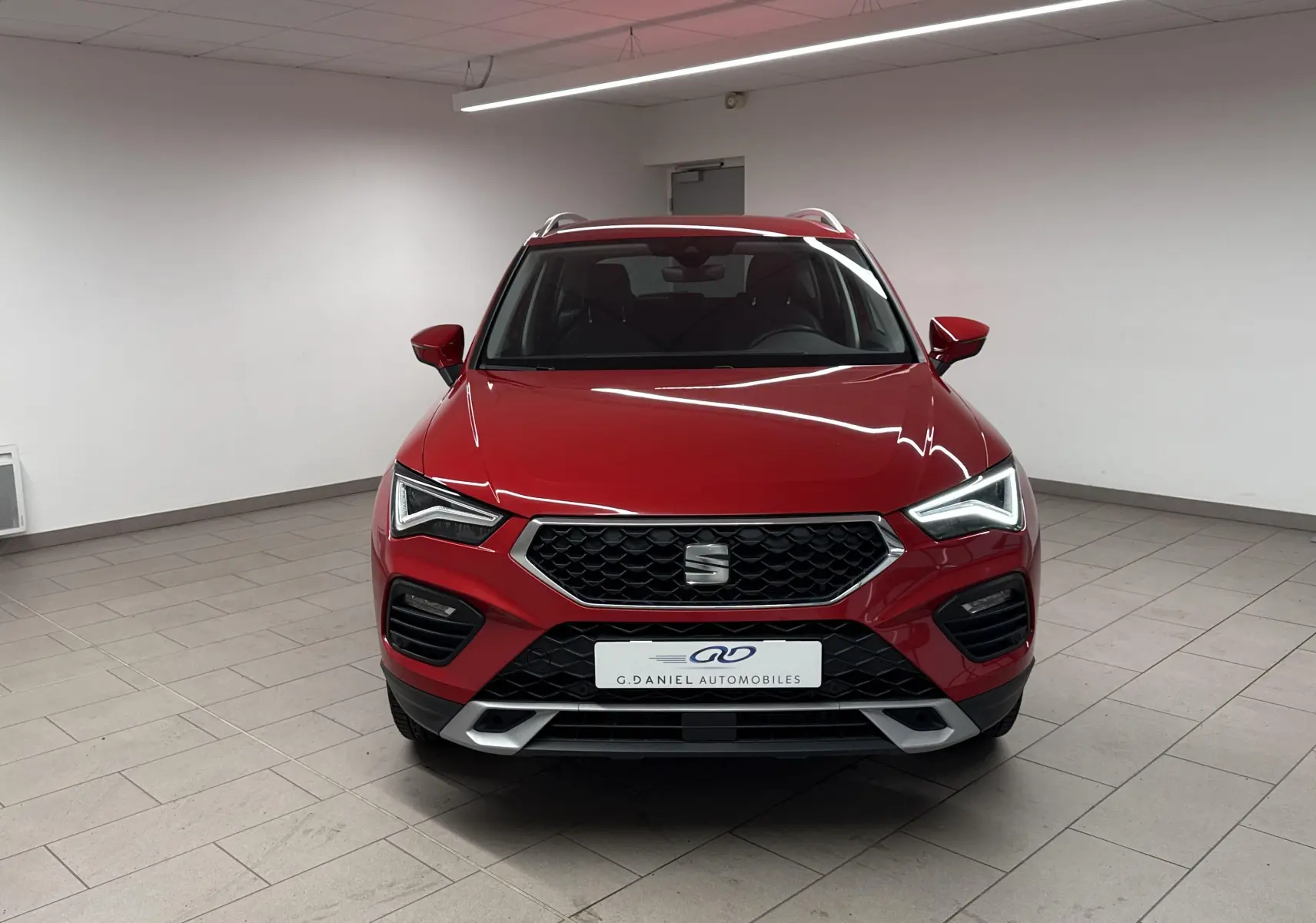 Vue frontale d'un SEAT Ateca 2024 en rouge velvet, avec calandre hexagonale et phares LED allumés dans un showroom.