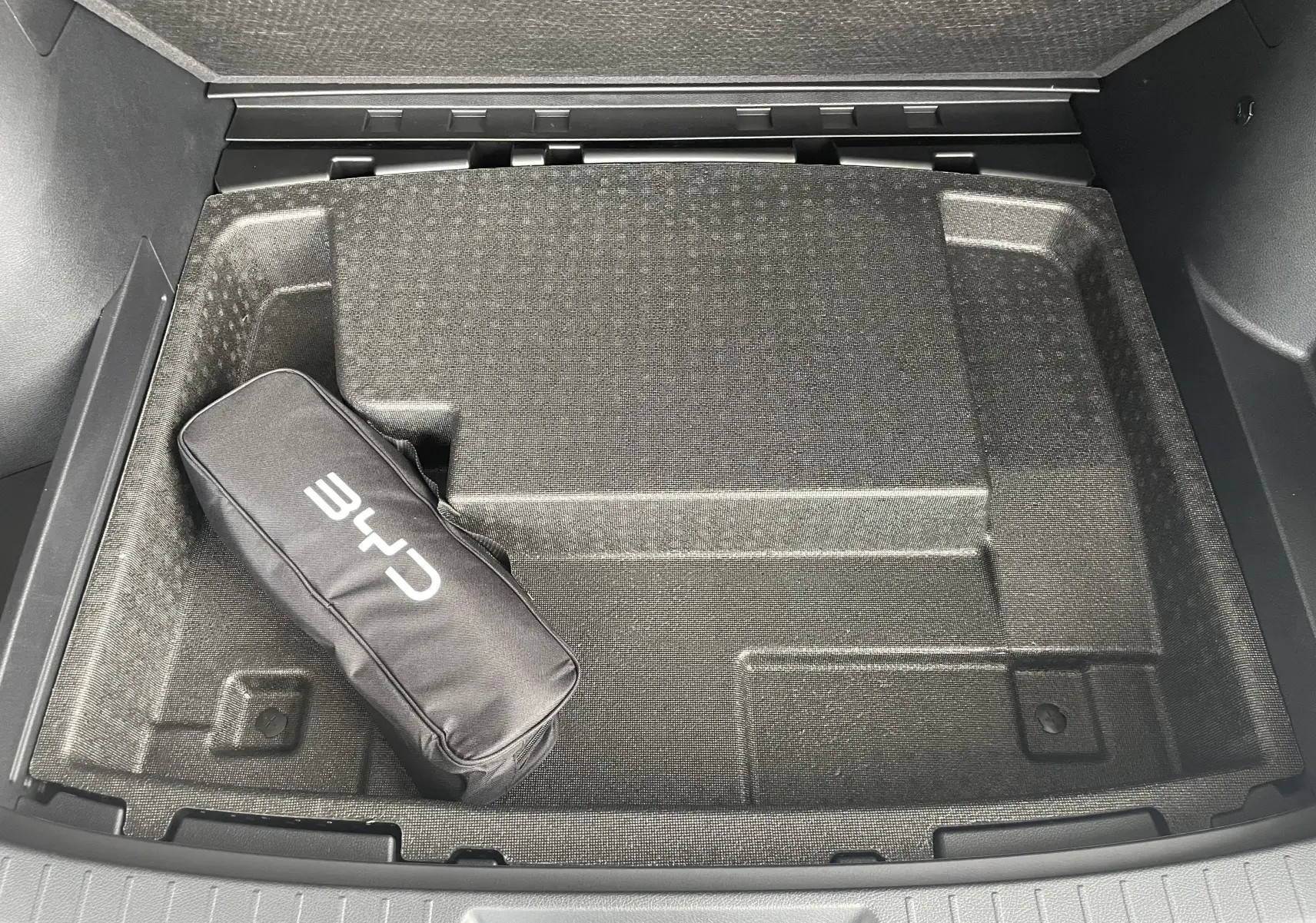 Vue plongeante sur le rangement sous plancher du coffre du BYD SEAL U 2026 en TIME GREY avec sacoche CHR noire.