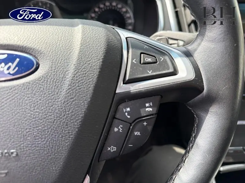 Gros plan sur le volant cuir noir du Ford Edge 2016 avec commandes multifonctions et logo Ford central.