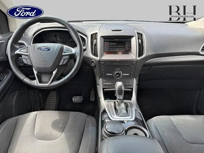 Vue intérieure avant du Ford Edge 2016 avec tableau de bord noir, volant multifonction et console centrale avec écran tactile.