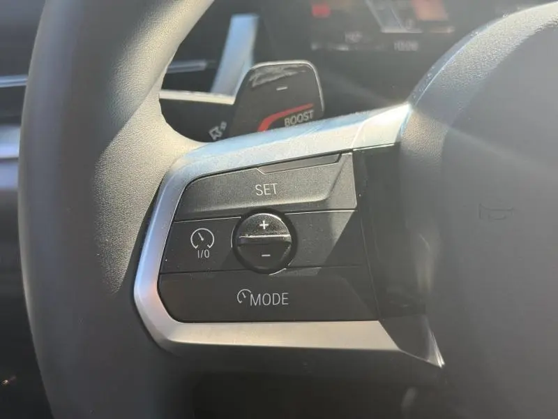 Gros plan sur les commandes de régulateur de vitesse au volant cuir du BMW X2 sDrive20dA gris Skyscraper.