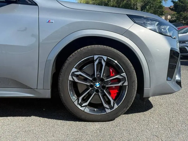Gros plan sur la roue avant droite d'une BMW X2 Skyscraper Grey métallisé avec étrier de frein rouge et logo M sur l'aile.