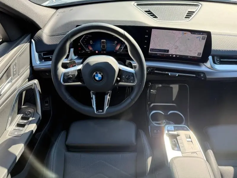 Vue intérieure avant du BMW X2 sDrive20dA 2025, volant cuir noir et écran tactile GPS intégré sur tableau de bord.
