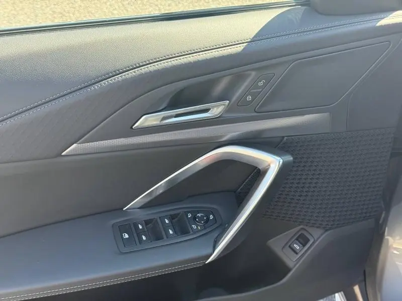 Détail de la porte avant gauche de la BMW X2 2025 en Skyscraper Grey, avec commandes de vitres et poignée argentée.