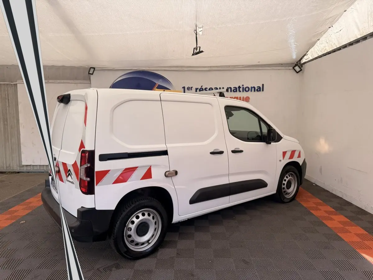Vue de côté droit arrière d’un Citroën Berlingo blanc avec bandes réfléchissantes rouges et blanches sur la carrosserie.