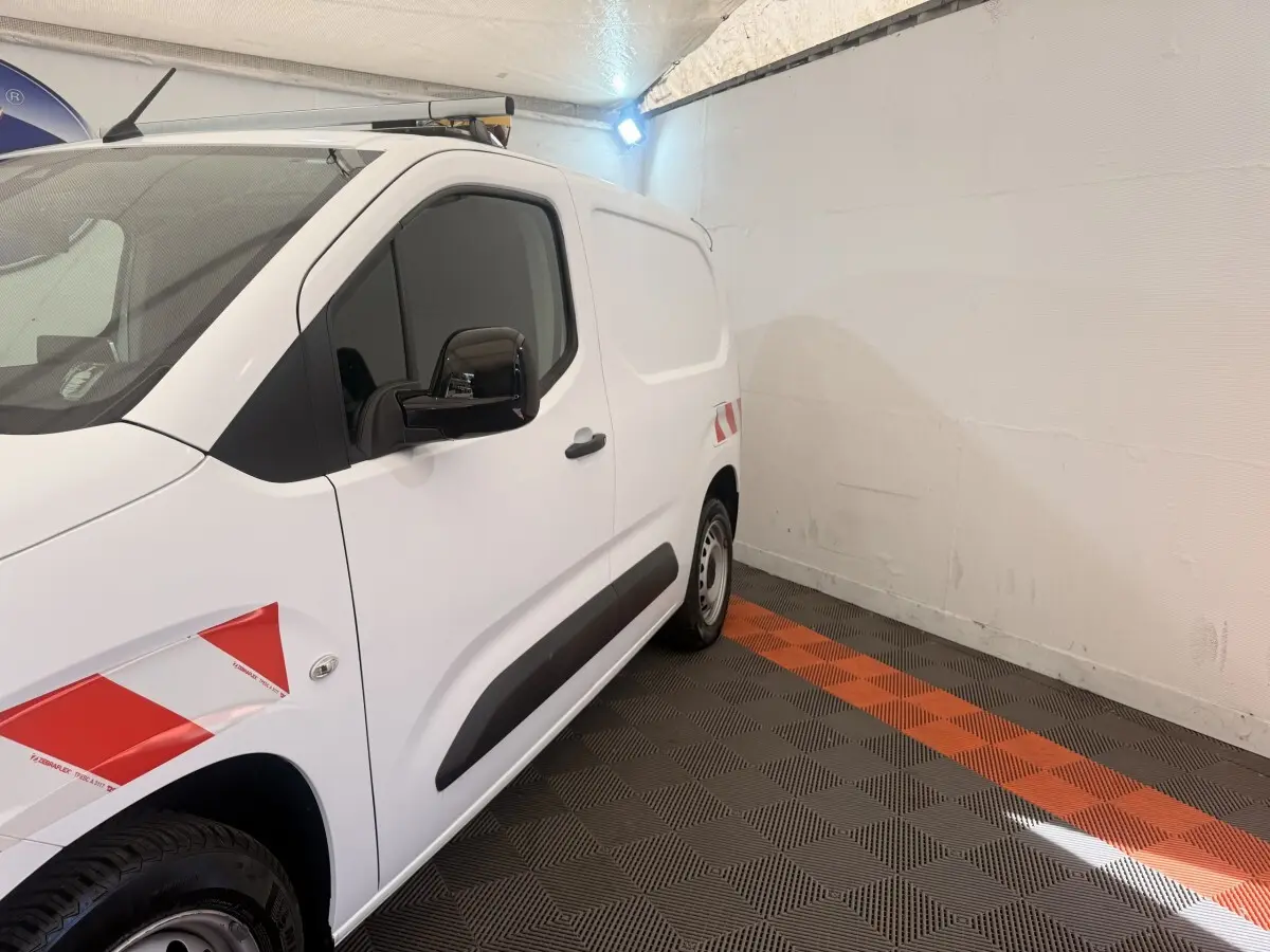 Vue de profil côté gauche d’un Citroën Berlingo blanc avec marquages rouges et protections noires sur porte.