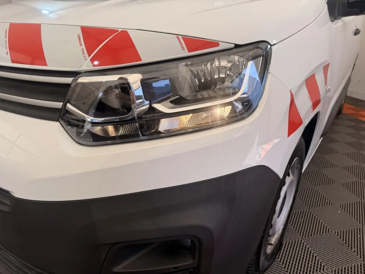 Gros plan sur l'avant droit blanc d'un Citroën Berlingo 2022 avec phare allumé et marquages rouges réfléchissants.