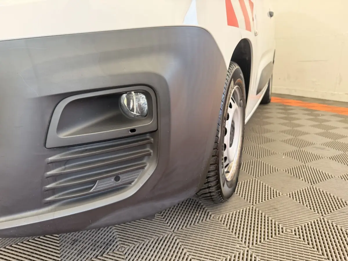 Gros plan sur l'antibrouillard avant droit et la roue acier du Citroën Berlingo blanc, vue de profil avant.