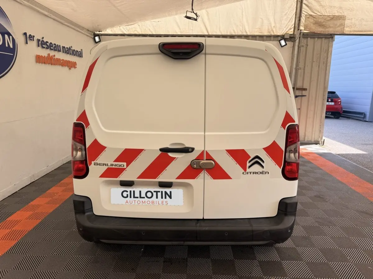 Vue arrière d’un Citroën Berlingo blanc avec bandes rouges réfléchissantes et logo constructeur visible.