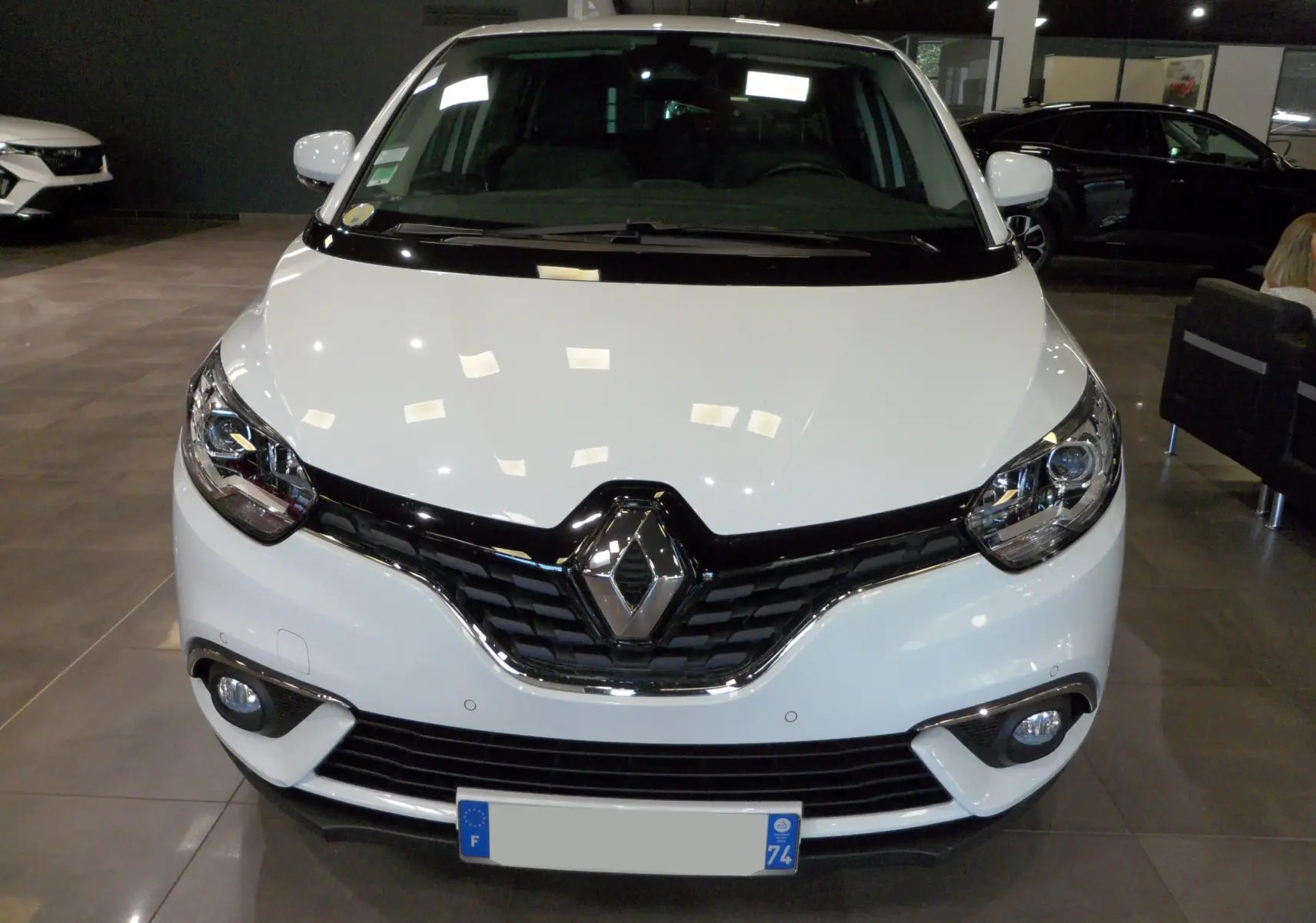 Vue frontale d'un Renault Grand Scenic IV blanc glacier en intérieur, avec calandre noire et phares allumés.