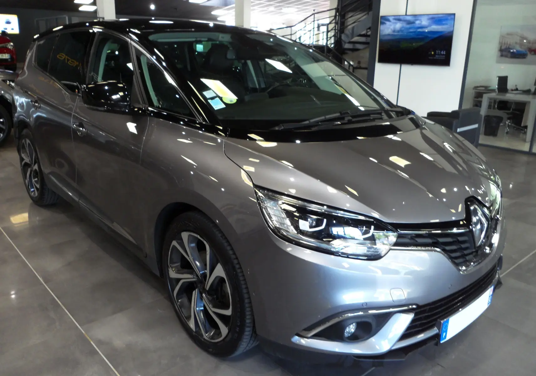 Vue 3/4 avant gauche du Renault Grand Scenic IV gris Cassiopé avec toit noir et jantes alliage distinctives.