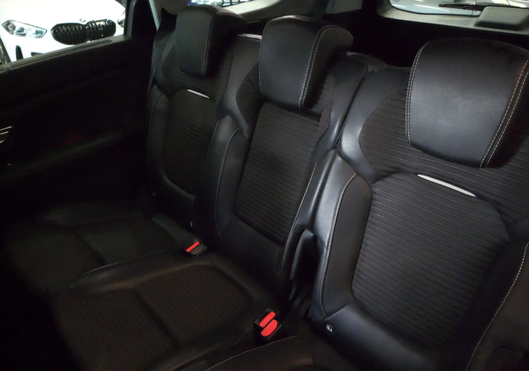 Vue rapprochée des sièges arrière en cuir noir du Renault Grand Scenic IV, soulignant les appuie-têtes et les ceintures rouges.