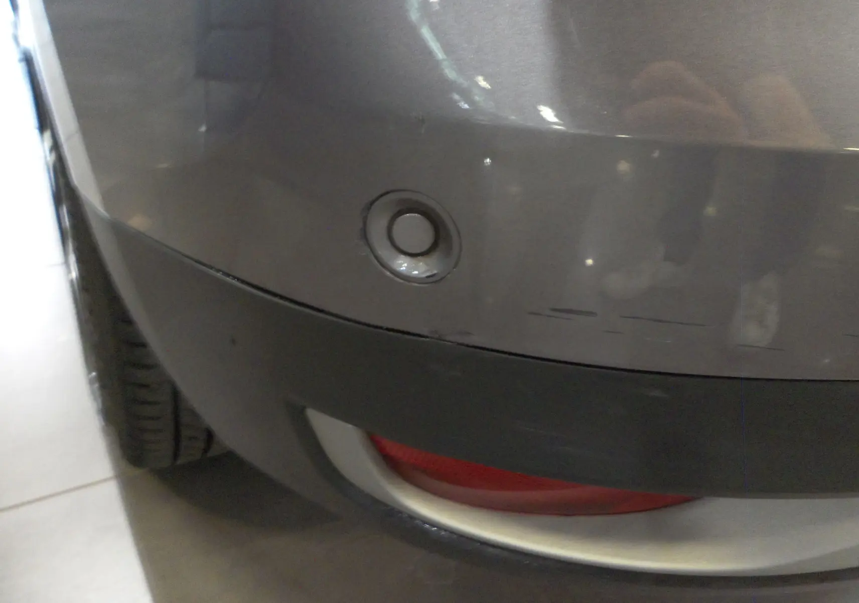 Gros plan sur le pare-chocs arrière gris cassiopé du Renault Grand Scenic IV avec capteur de recul visible.