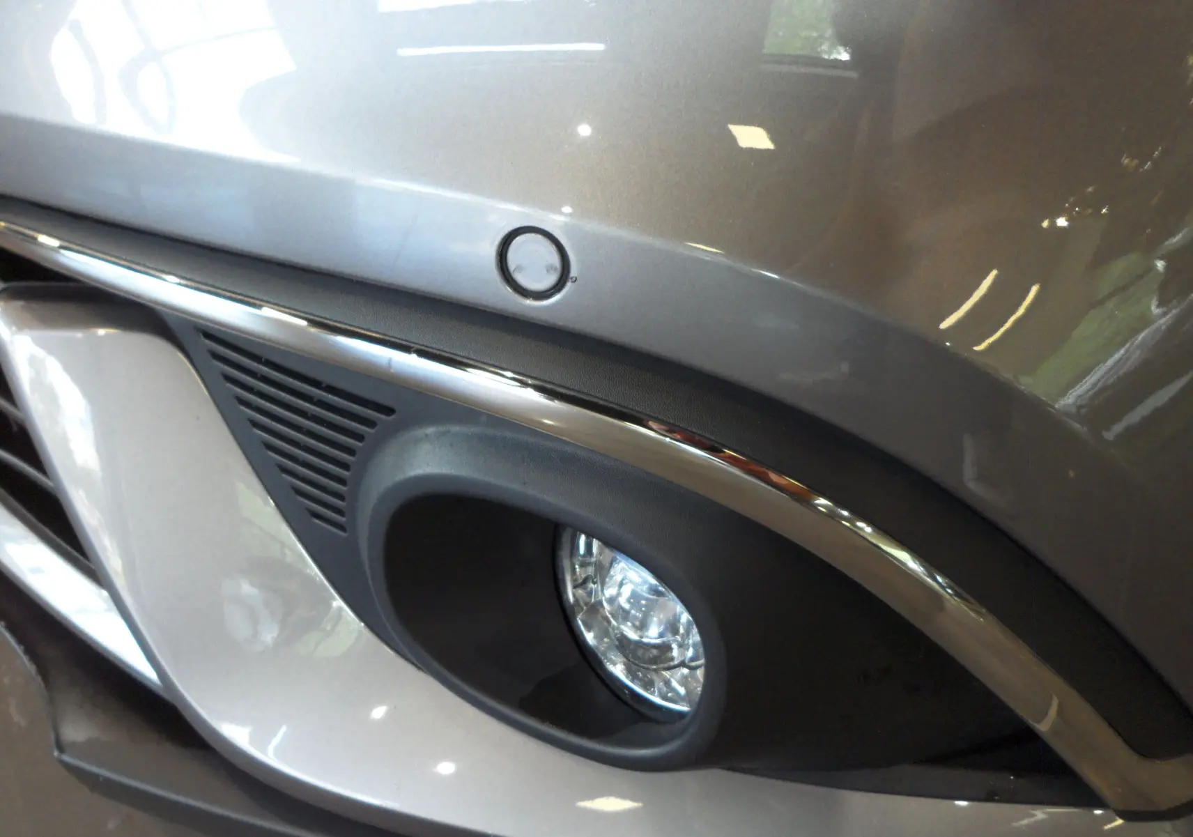 Gros plan sur le feu antibrouillard avant droit du Renault Grand Scenic IV gris Cassiopé avec détails chromés.