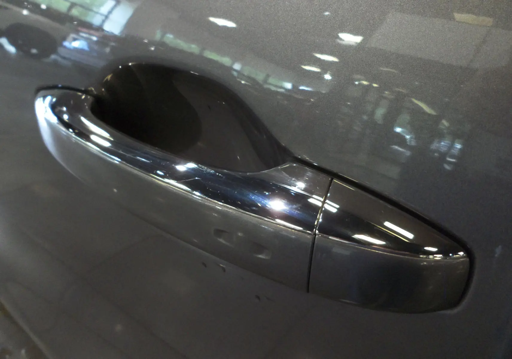 Poignée de porte avant droite chromée sur Renault Grand Scenic IV gris Cassiopé avec reflet intérieur showroom.