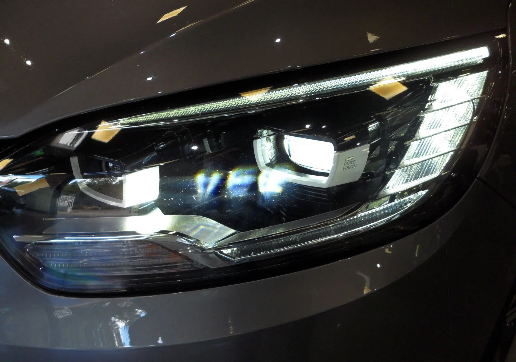 Gros plan sur le phare avant droit du Renault Grand Scenic IV gris Cassiopé avec éclairage LED Pure Vision.