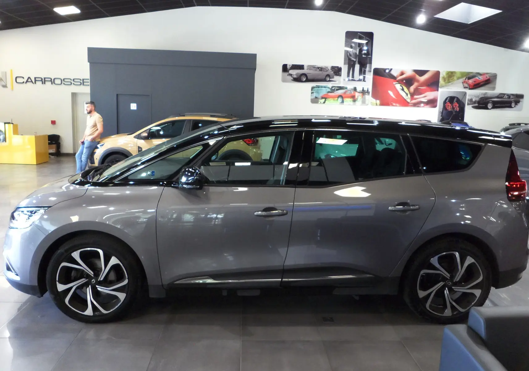 Profil côté gauche du Renault Grand Scénic IV gris Cassiopé avec toit noir, roues alliage et vitres teintées en showroom.