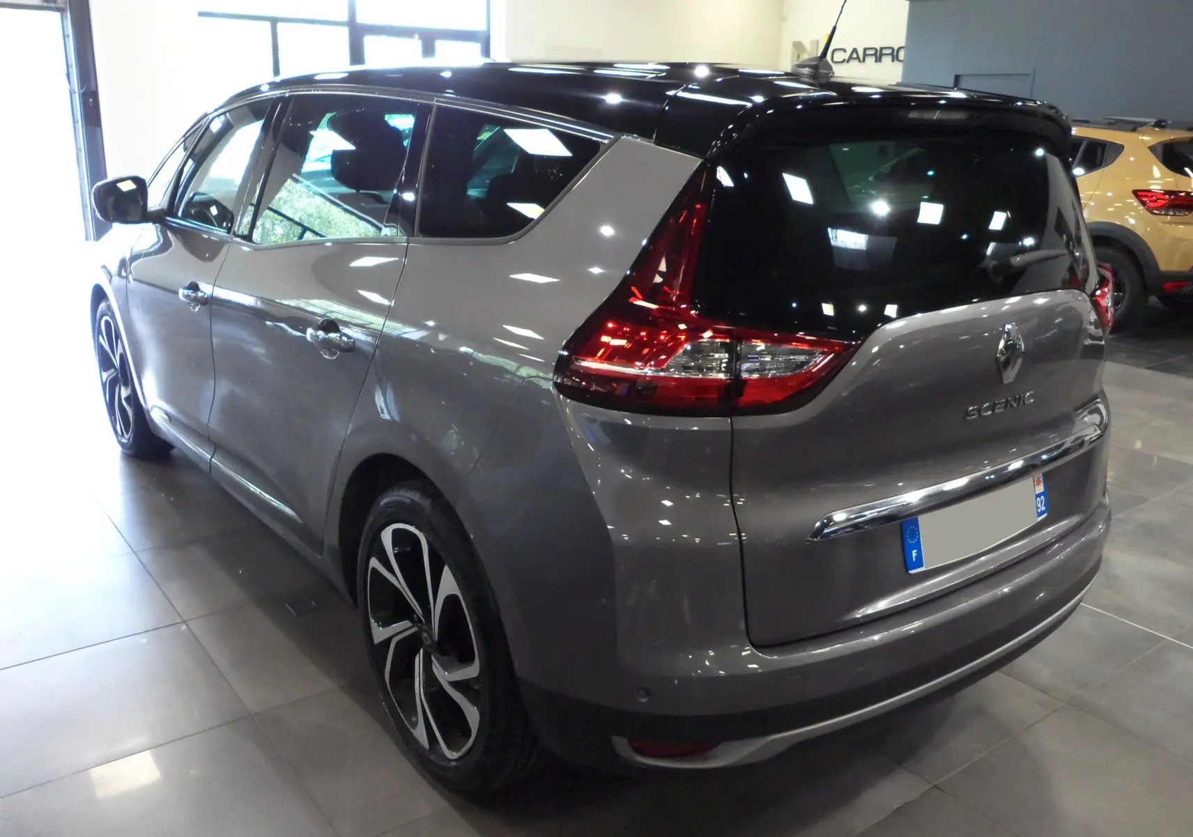 Vue 3/4 arrière droit d'un Renault Grand Scenic IV gris Cassiopé avec toit noir et jantes distinctives en concession.