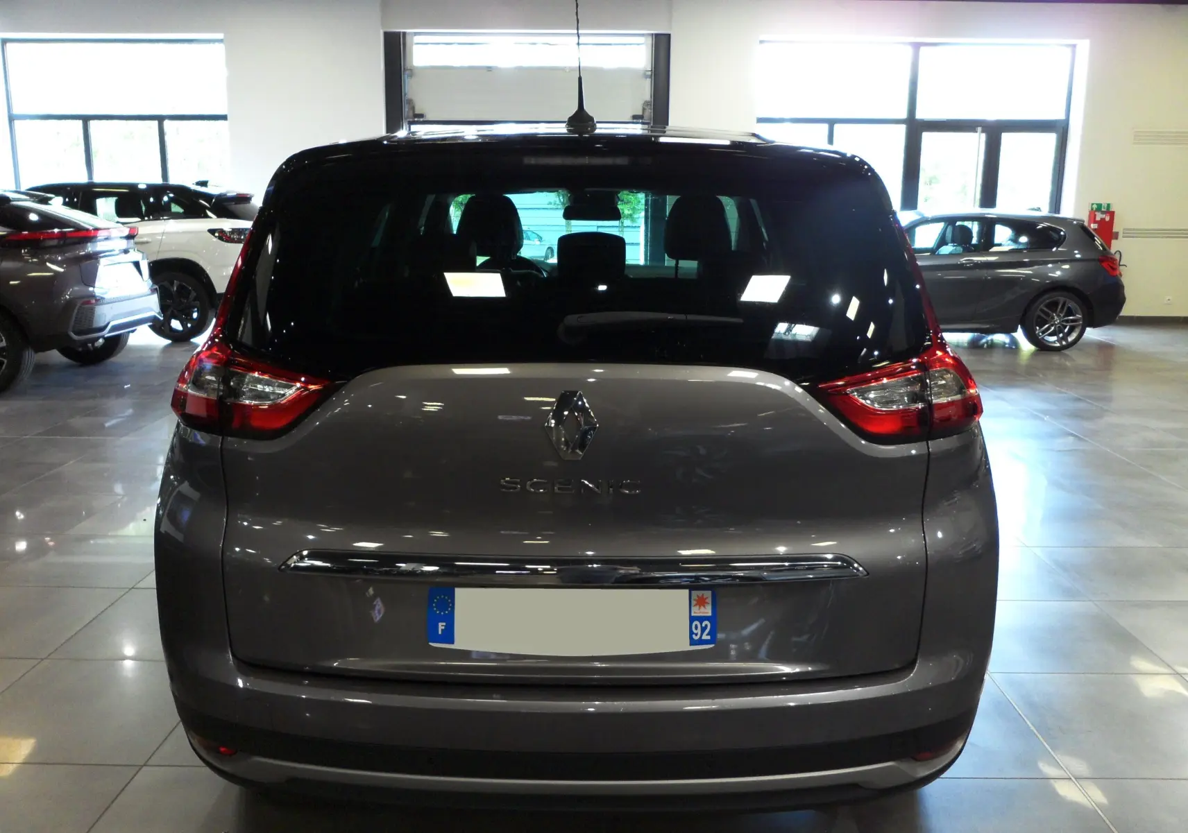 Vue arrière d'un Renault Grand Scenic IV gris Cassiopé avec toit noir, dans un showroom lumineux.