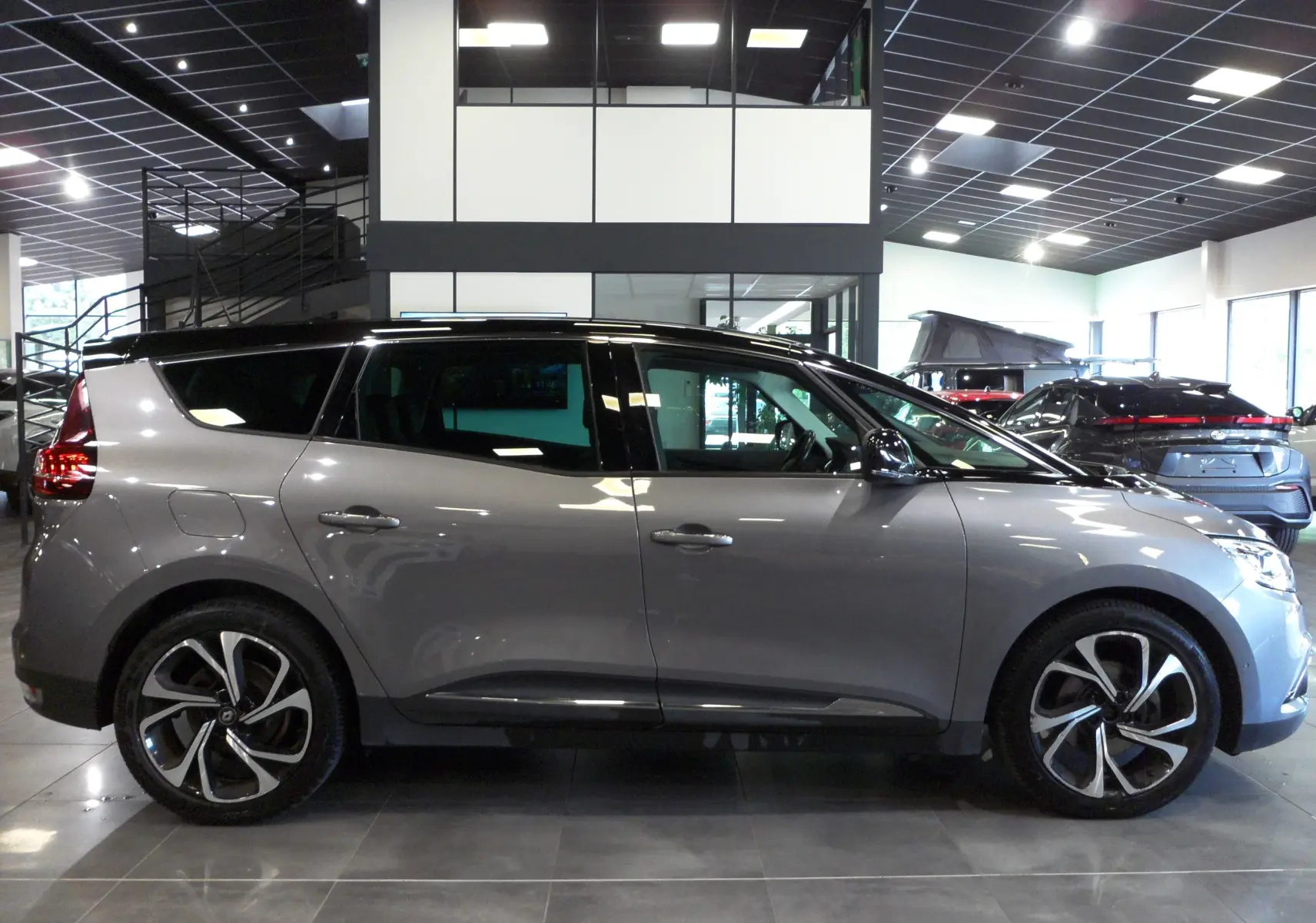 Profil droit du Renault Grand Scenic IV gris Cassiopé avec toit noir, jantes alliage et intérieur visible en showroom.