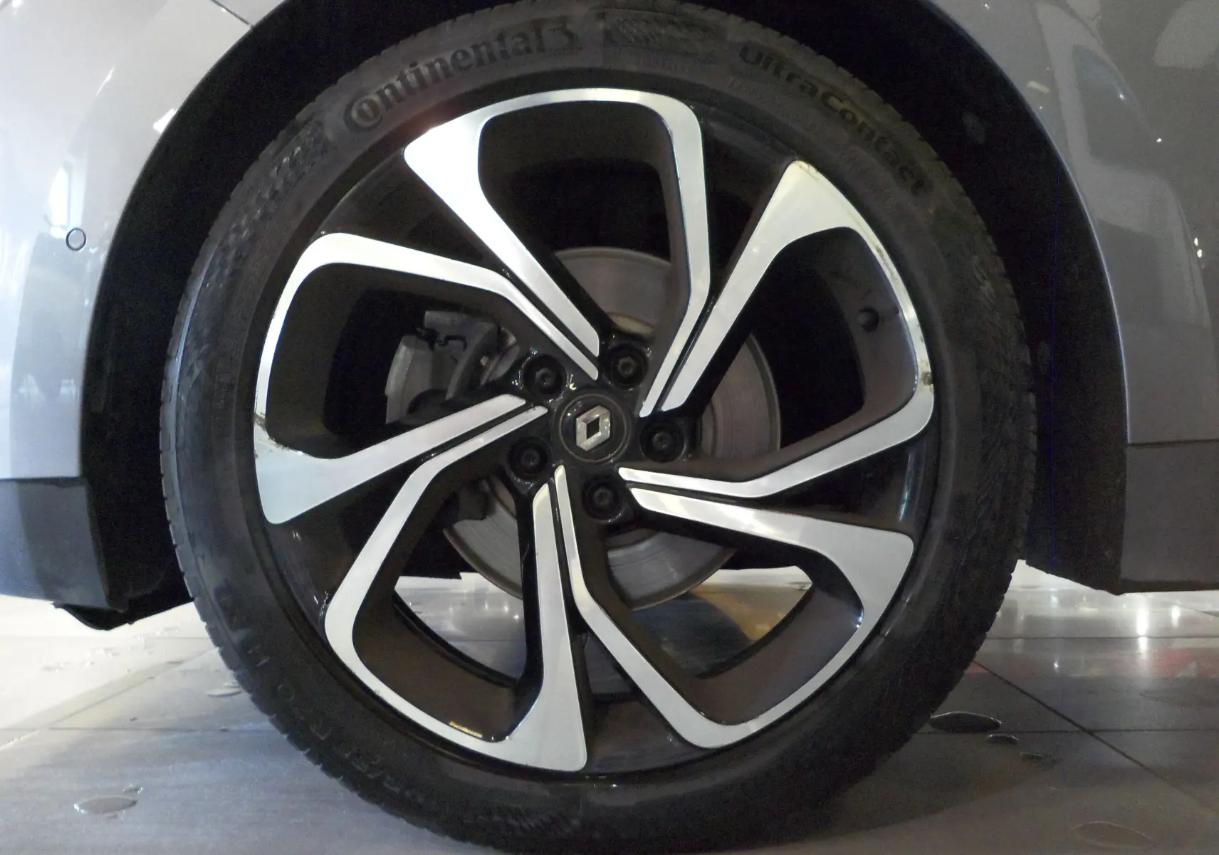 Gros plan sur la roue avant gauche du Renault Grand Scenic IV gris Cassiopé, jante alliage bicolore moderne.