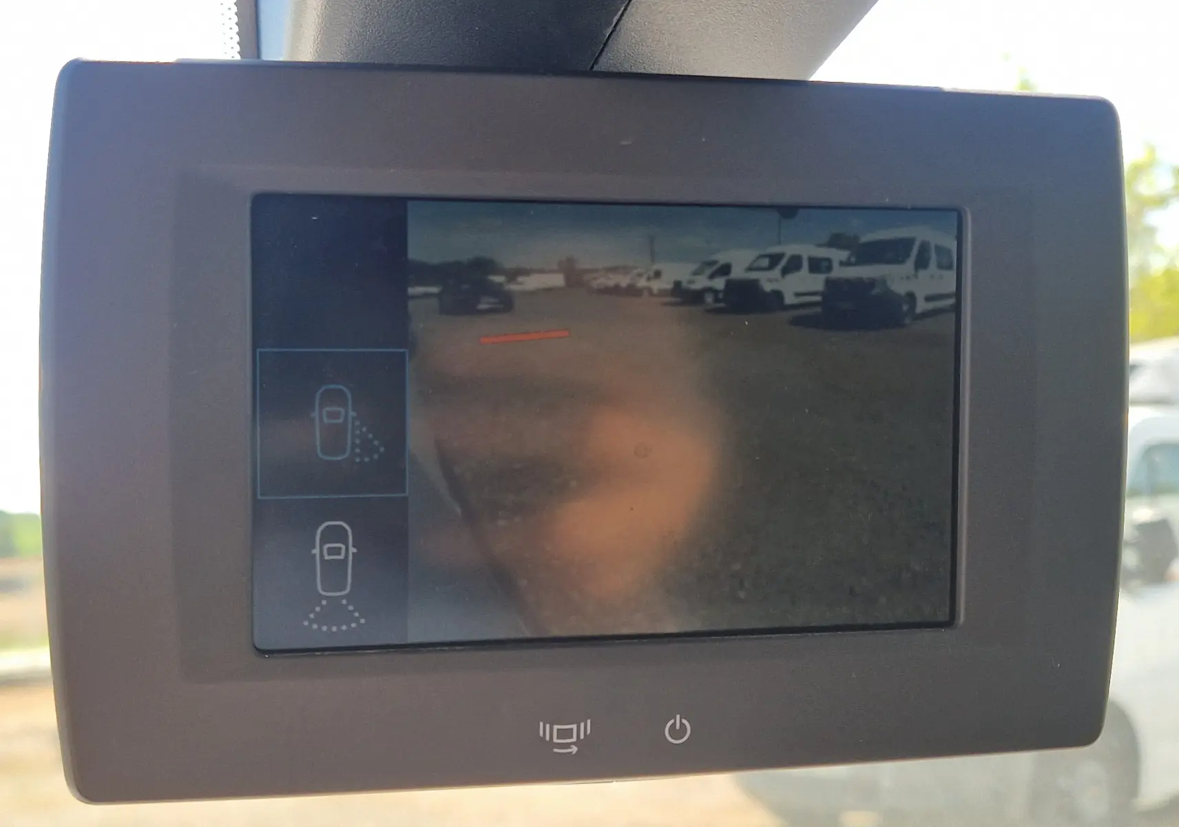 Écran de caméra de recul montrant un parking avec plusieurs véhicules utilitaires blancs, vue depuis l'intérieur du Citroën Berlingo blanc.