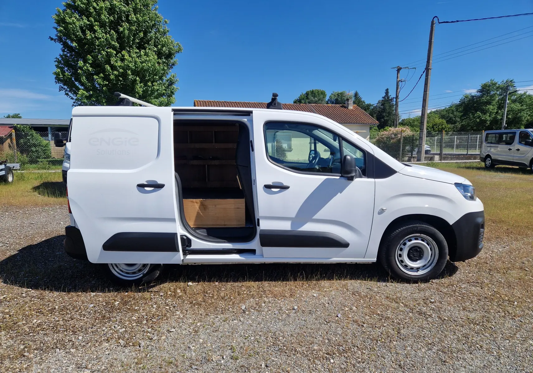 Vue de profil droit d'un Citroën Berlingo blanc 2020 avec porte coulissante ouverte montrant l'intérieur utilitaire en bois.
