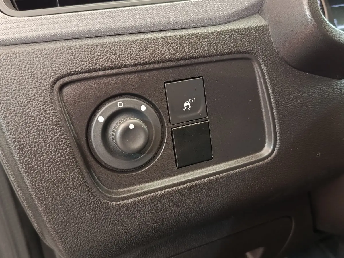 Gros plan sur les commandes de réglage des phares et de l'antipatinage dans le tableau de bord noir du Renault Express blanc.