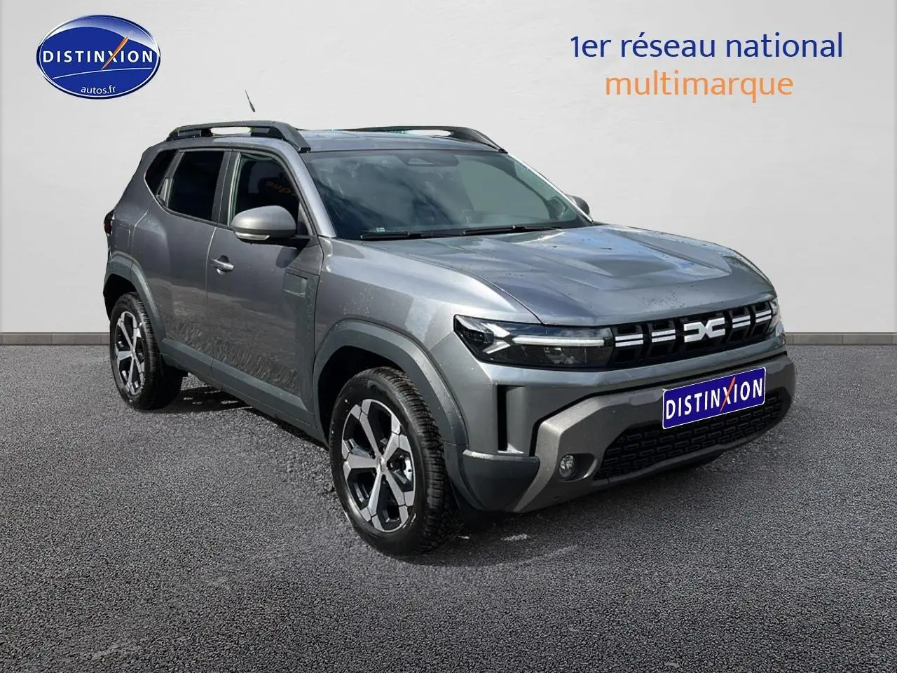 SUV Dacia Duster gris schiste en 3/4 avant droit avec jantes alu et barres de toit visibles.