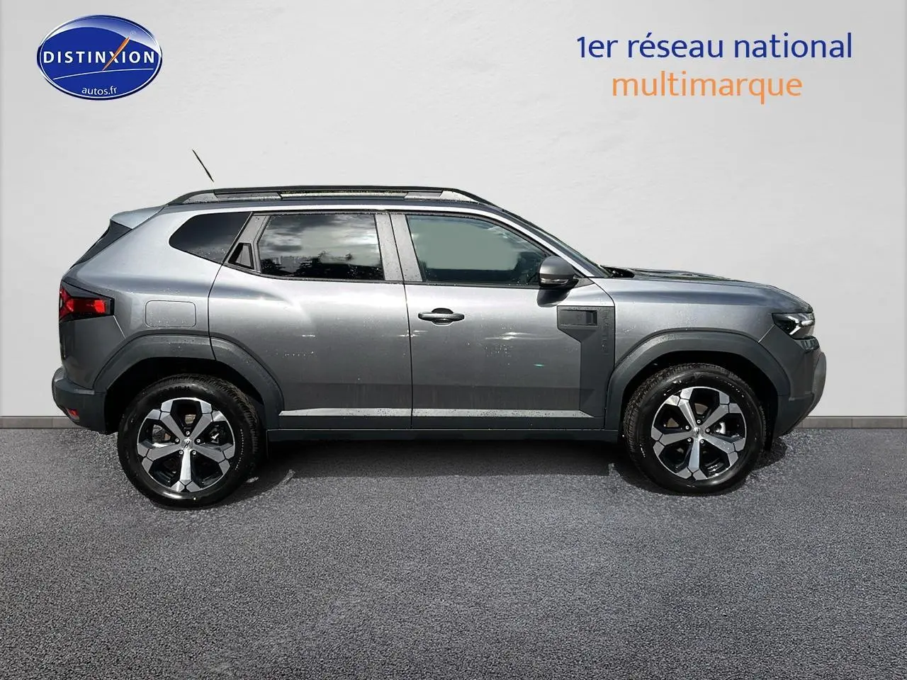 Profil droit du Dacia Duster gris schiste 2025 avec jantes alu et barres de toit visibles.