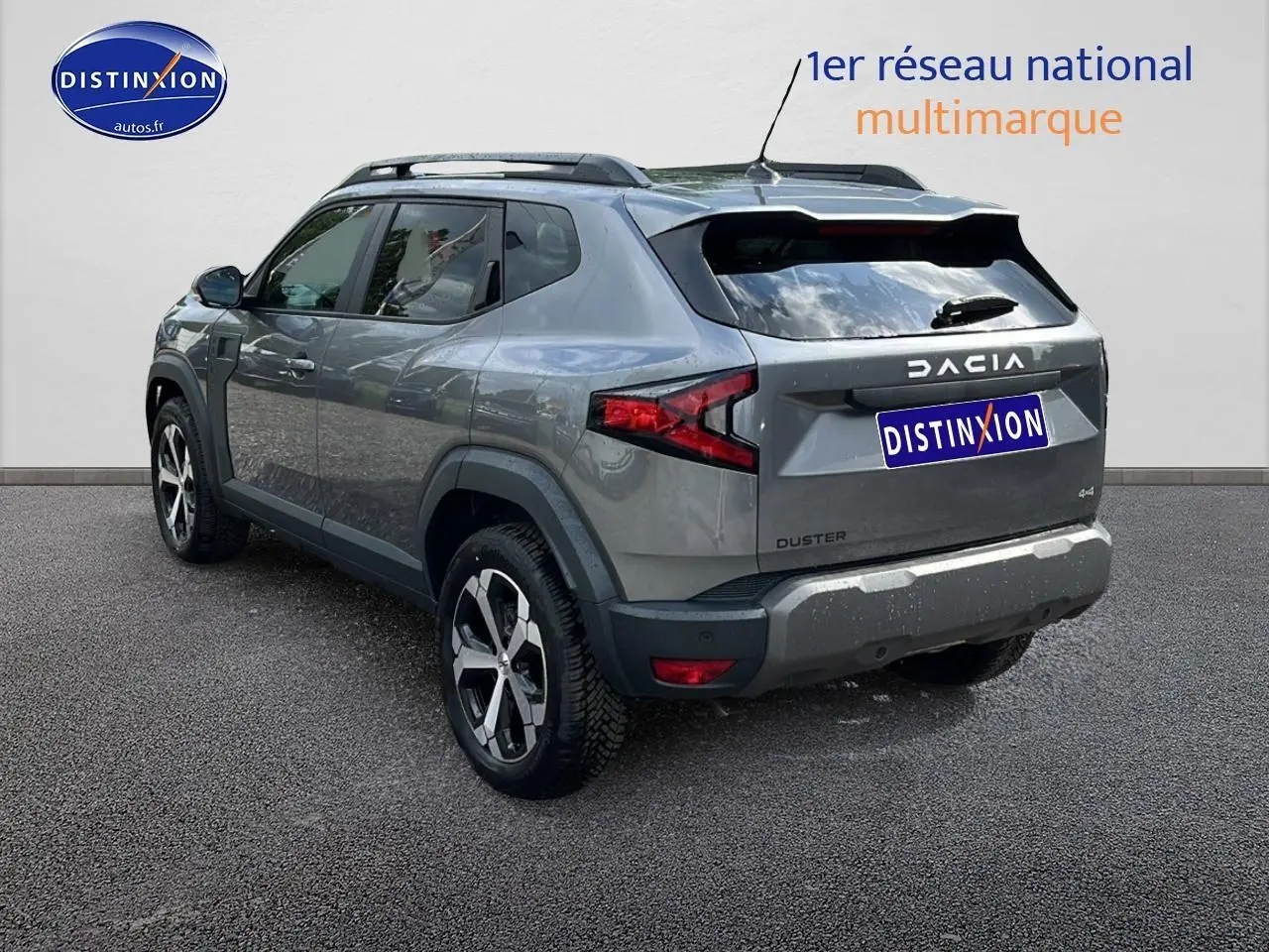 Vue 3/4 arrière droite d'un Dacia Duster gris schiste avec barres de toit et jantes alu distinctives.