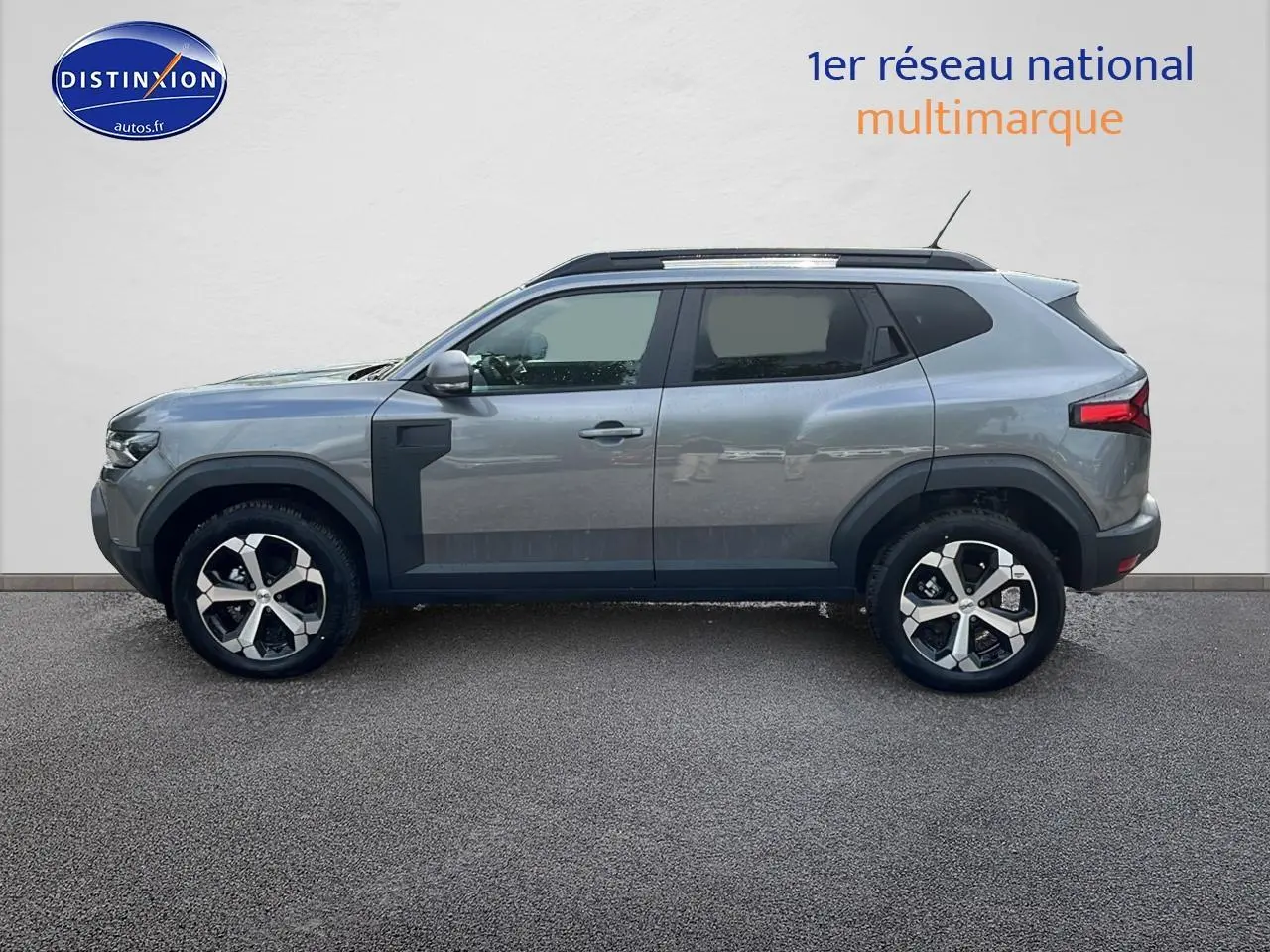 Profil droit du Dacia Duster gris schiste 2025 avec jantes alu et barres de toit noires visibles.