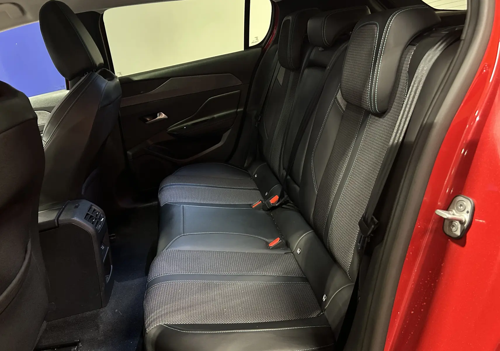 Vue intérieure arrière côté droit du Peugeot 308 2024 rouge, montrant les sièges arrière en cuir et tissu noir.