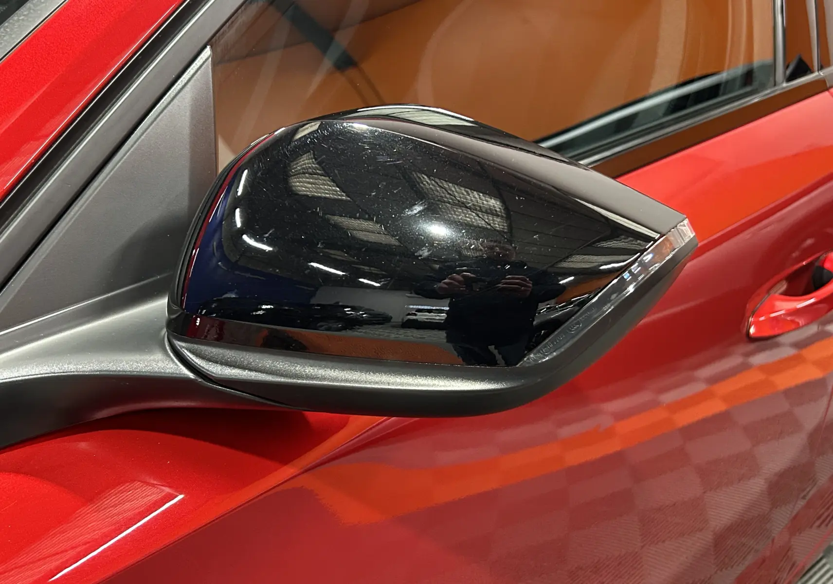 Rétroviseur noir côté gauche en gros plan sur Peugeot 308 rouge 2024, avec porte et vitre visibles en arrière-plan.