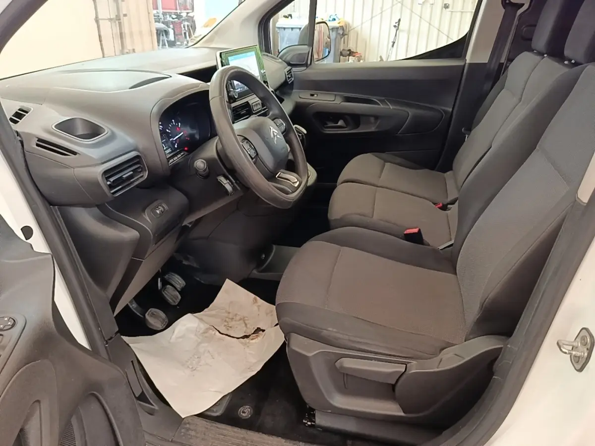Intérieur côté conducteur du Citroën Berlingo blanc, montrant le volant multifonctions et les sièges tissu gris.