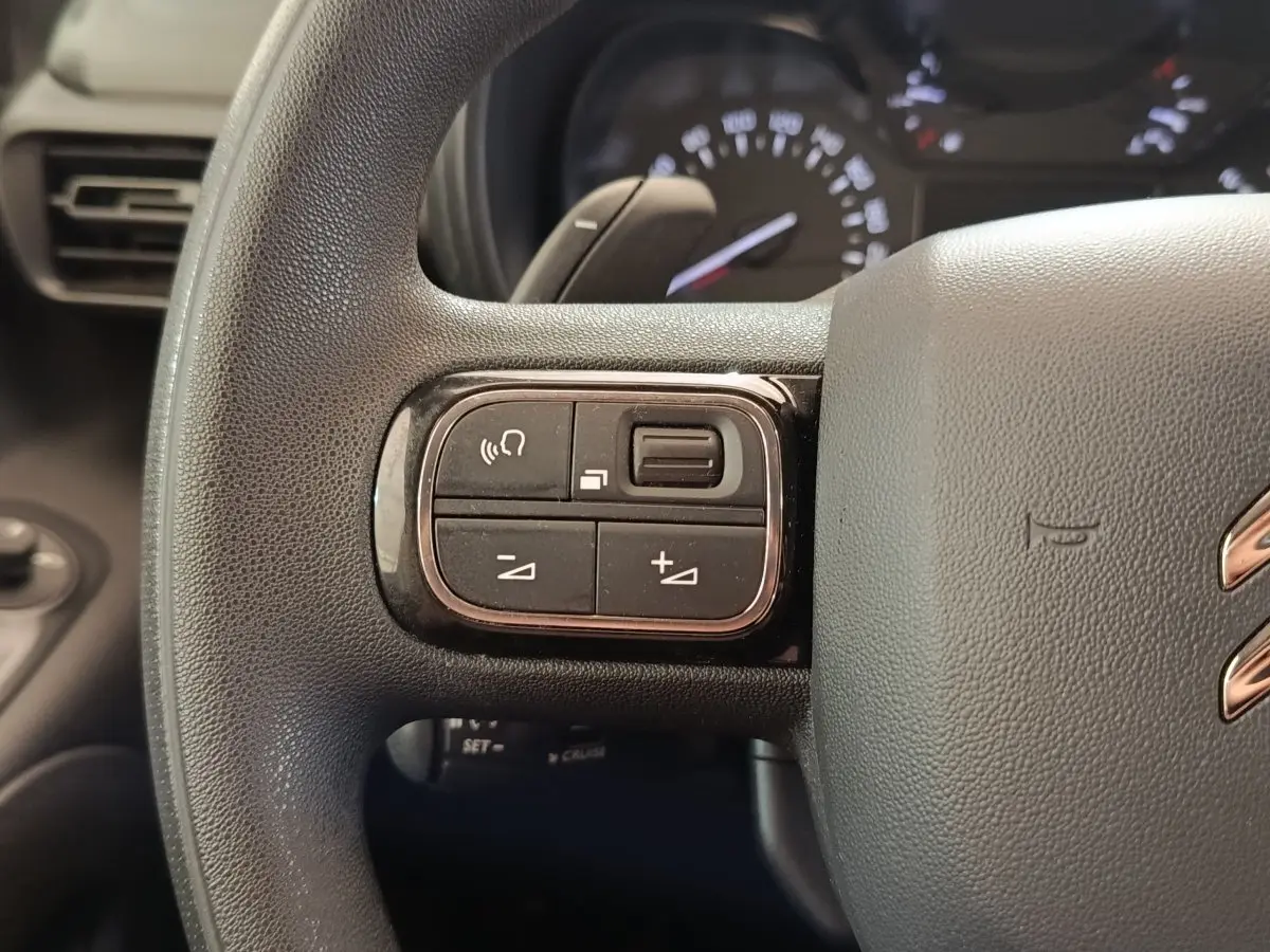 Gros plan sur le volant multifonctions noir du Citroën Berlingo blanc, avec commandes audio et téléphone visibles.