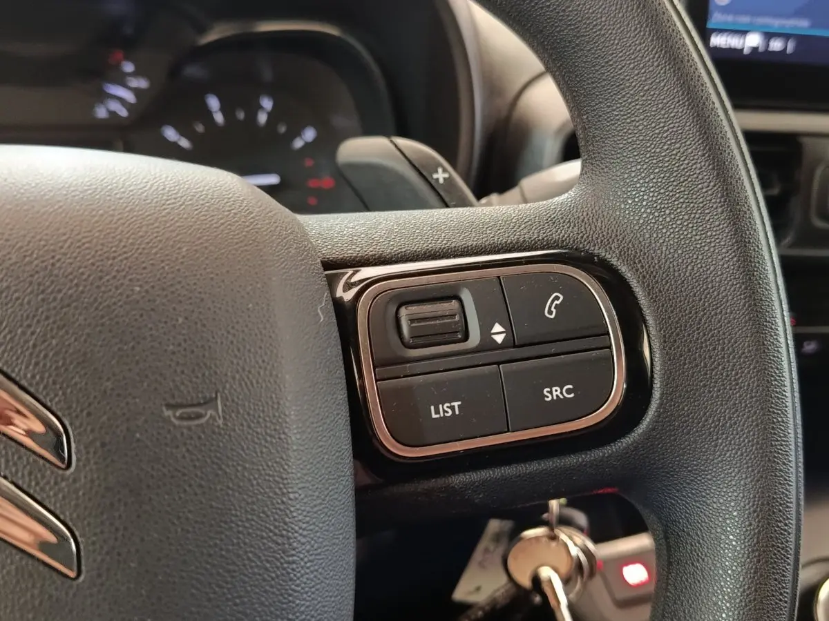 Gros plan sur le volant multifonctions noir du Citroën Berlingo blanc, avec commandes audio et téléphone visibles.