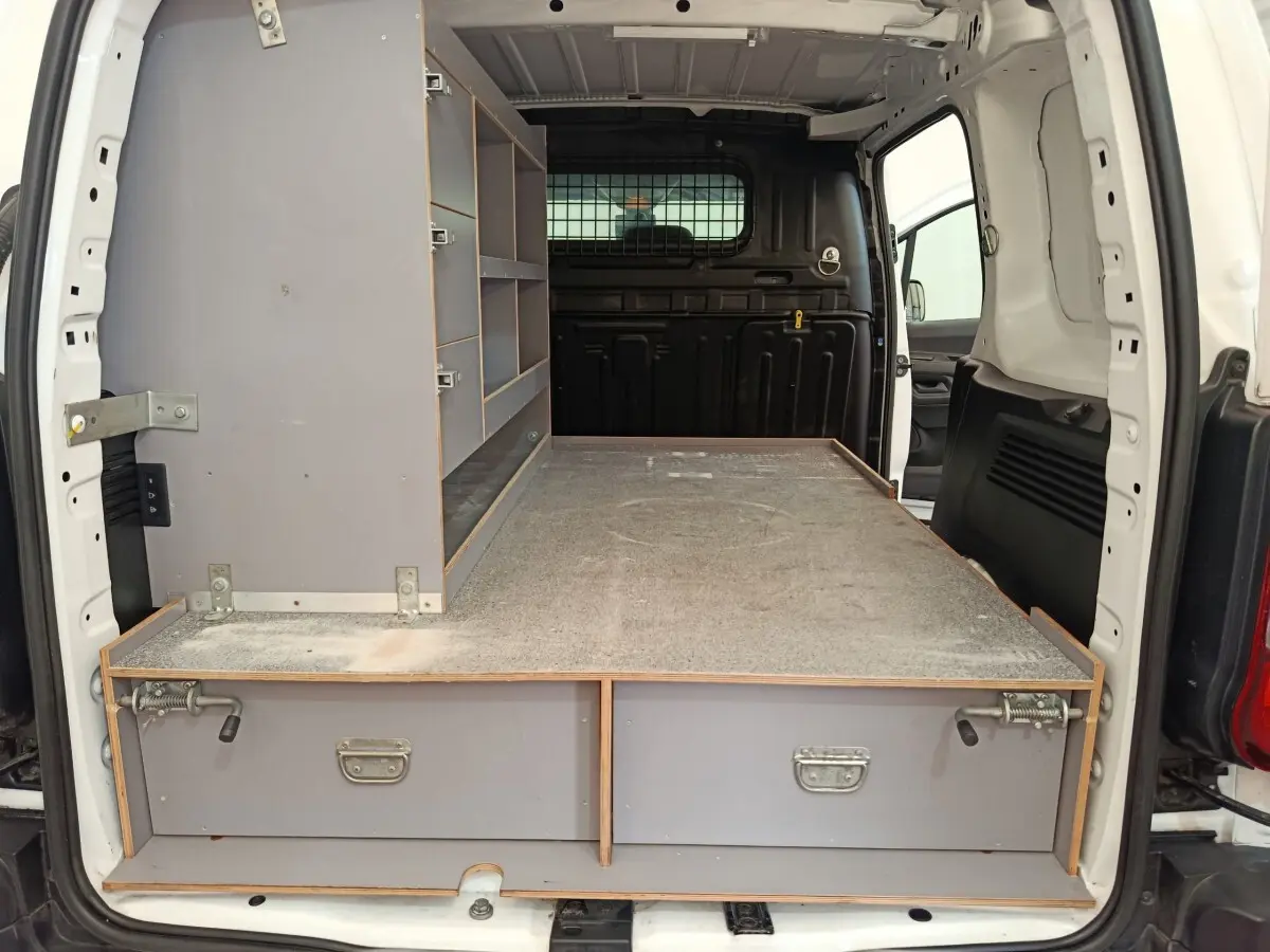 Vue arrière ouverte du Citroën Berlingo blanc, montrant l'aménagement intérieur avec étagères et plateau de rangement gris.
