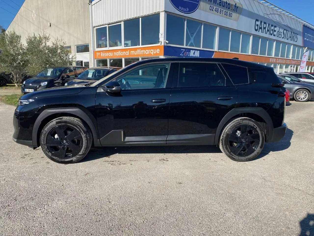 Vue de profil côté gauche d'un Citroën C5 Aircross noir avec jantes alliage noires, stationné devant un garage.