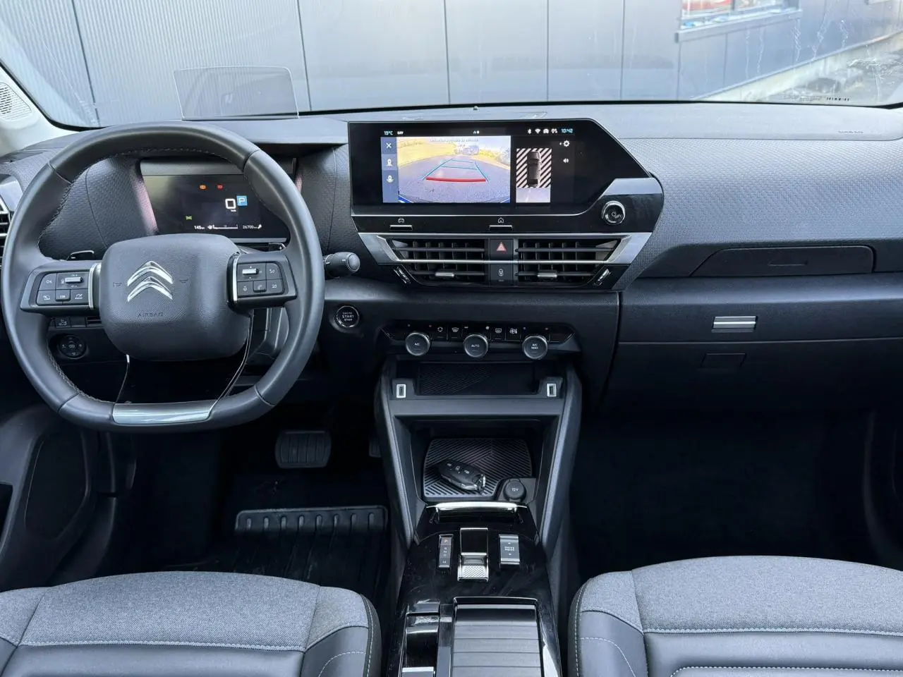 Vue intérieure avant du Citroën C4 X 2024 noir Perla, tableau de bord avec écran tactile et caméra de recul affichée.