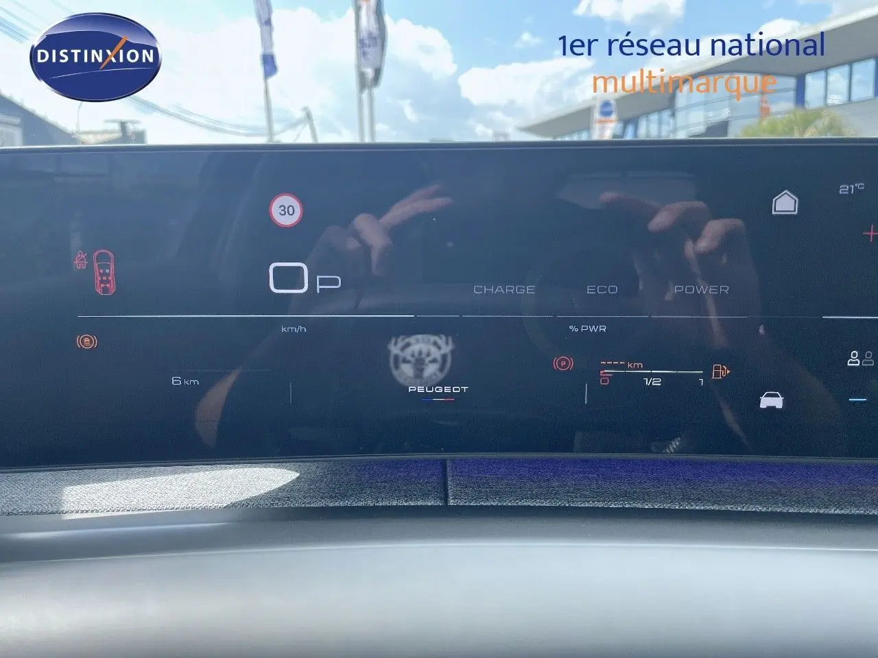 Tableau de bord numérique du Peugeot 5008 Hybrid 2025 affichant la vitesse et l'autonomie, avec reflet extérieur.
