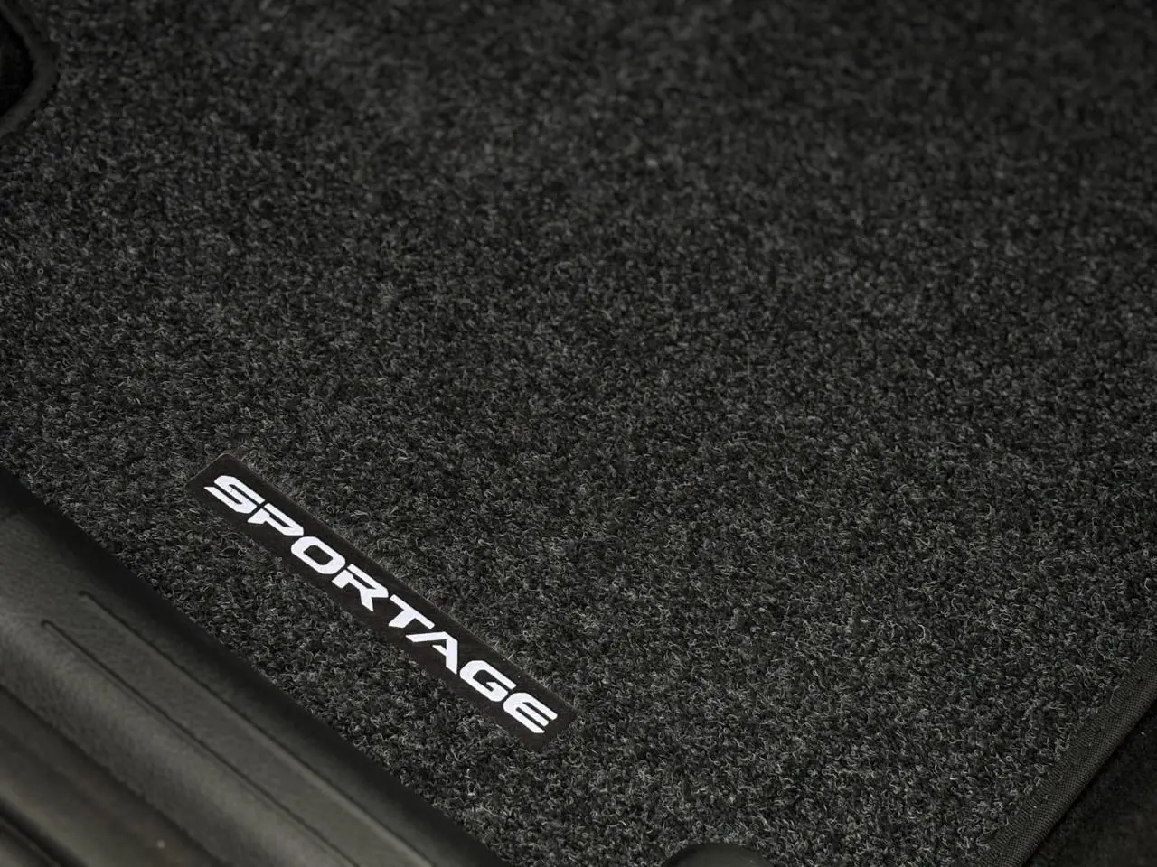 Gros plan sur le tapis de sol noir avec l'inscription blanche "SPORTAGE" du KIA Sportage 2025 gris perle.