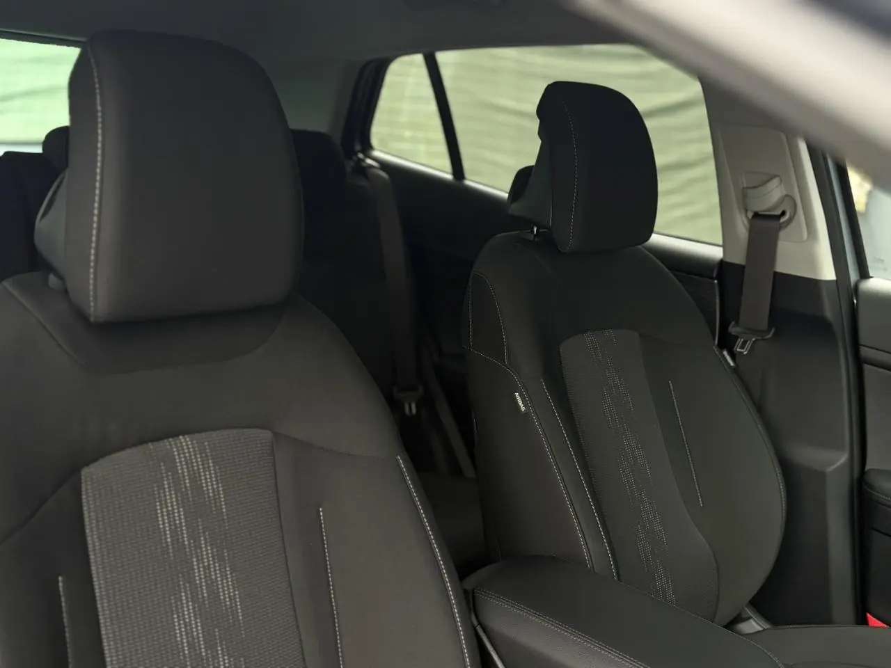 Gros plan sur les sièges avant noirs du Kia Sportage 2025 avec coutures contrastées et accoudoir central.